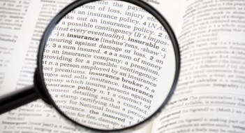 Magnifying glass focussed on the word 'insurance' on the page of a generic dictionary.