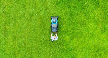 Beautiful girl cuts the lawn. Mowing lawns. Aerial view beautiful woman lawn mower on green grass. Mower grass equipment. Mowing gardener care work tool. Close up view. Aerial lawn mowing