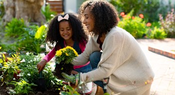 Happy african american mother and daughter planting flowers. family time, having fun together at home and garden.