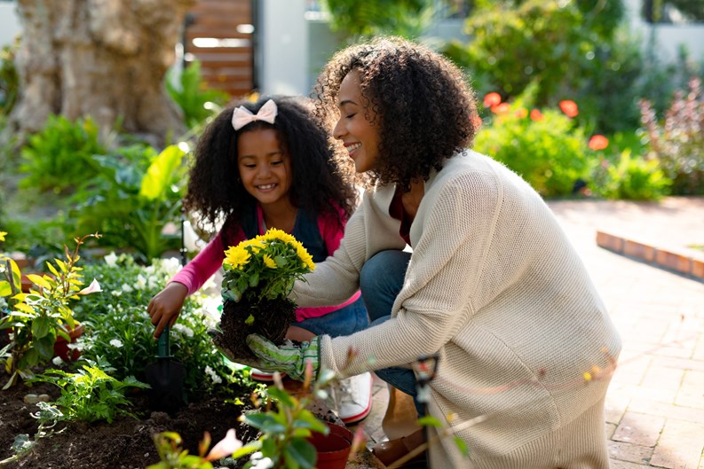 Happy african american mother and daughter planting flowers. family time, having fun together at home and garden.