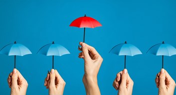 Hand with miniature red umbrella isolated on blue background protect concept. Close up of different women hands holding little tiny blue umbrellas against while a red one differentiate itself. Investment protection and insurance concept, differentiate yourself from the crowd.