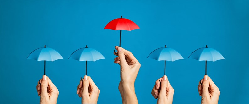 Hand with miniature red umbrella isolated on blue background protect concept. Close up of different women hands holding little tiny blue umbrellas against while a red one differentiate itself. Investment protection and insurance concept, differentiate yourself from the crowd.