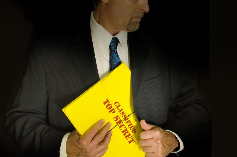 Top Secret Classified business, legal and government concept showing a man in a black suit pulling a Top Secret folder dossier out of his jacket. Dramatic lighting highlights the Top Secret folder.