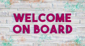 3D letters reading WELCOME ON BOARD in dark purple on a bright brick wall, with some colored paint-splatter.