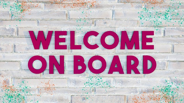 3D letters reading WELCOME ON BOARD in dark purple on a bright brick wall, with some colored paint-splatter.