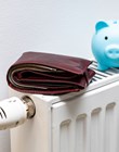 A stuffed wallet lying on the radiator and a small blue piggy bank, The concept of rising apartment heating costs