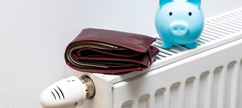 A stuffed wallet lying on the radiator and a small blue piggy bank, The concept of rising apartment heating costs