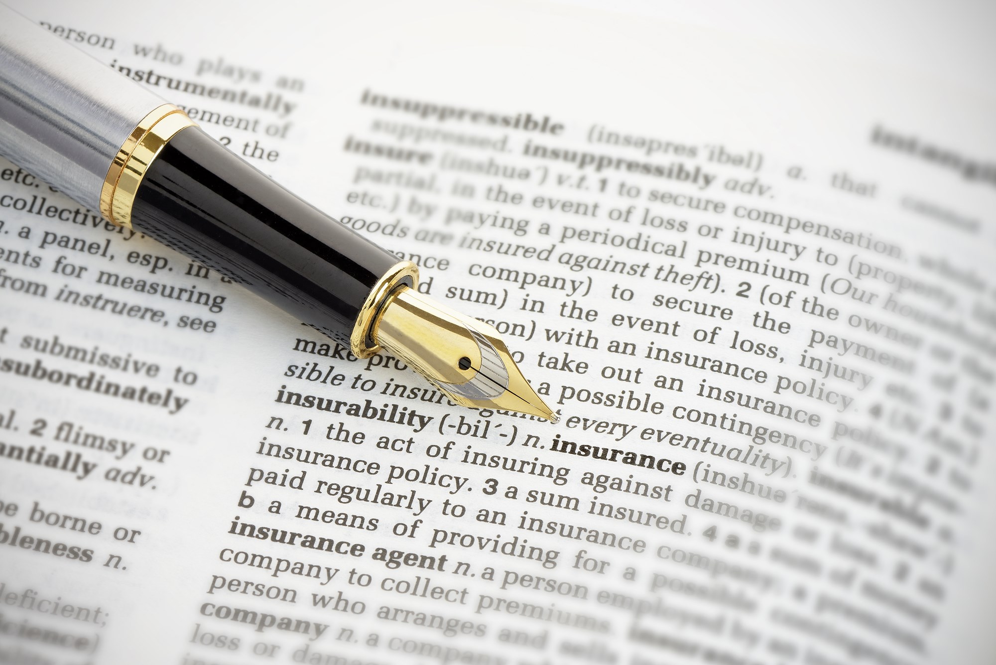 Fountain pen pointing to the word 'insurance' on the page of a generic dictionary.