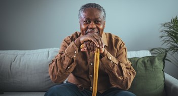 Managing Aging Residents Portrait of happy senior man smiling at home while holding walking cane. Old man relaxing on sofa and looking at camera. Portrait of elderly man enjoying retirement.