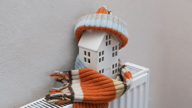 Figure of house and warm clothes on heating radiator. Home heating expenses and savings concept.