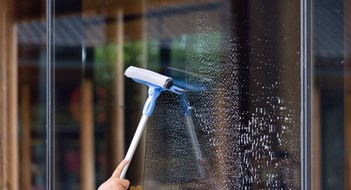 Façade Cleaning A person is cleaning a window with a squeegee. The window is covered in streaks and the person is using a blue and white squeegee to clean it