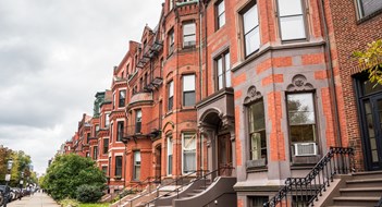 New England’s Condos, HOAs & Co-ops Row of old red-brick apartment buildings with staircases to the front doors along a tree lined street on a cloudy autumn day. Boston, MA, USA.