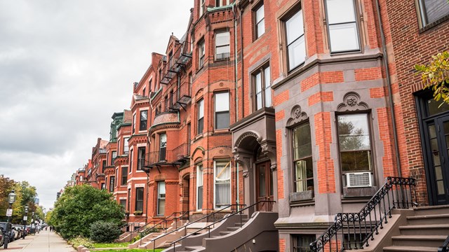Row of old red-brick apartment buildings with staircases to the front doors along a tree lined street on a cloudy autumn day. Boston, MA, USA.