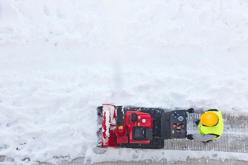 Worker cleaning snow on the sidewalk with a snowblower. Maintenance