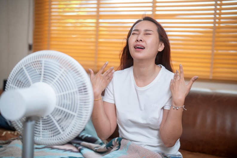Sweating Asian girl cooling herself with big fan